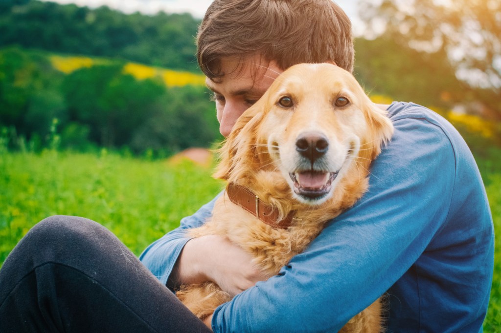 Homme serrant son Golden Retriever dans ses bras à l'extérieur.